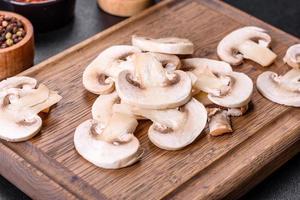 Beautiful young white champignons torn to slices on a dark concrete background photo