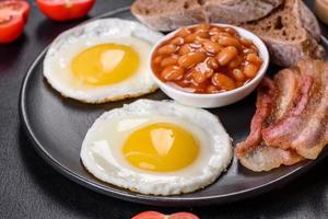 English breakfast with fried eggs, bacon, beans, tomatoes, spices and herbs photo