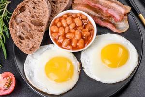English breakfast with fried eggs, bacon, beans, tomatoes, spices and herbs photo