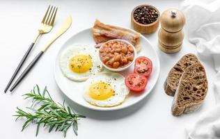 English breakfast with fried eggs, bacon, beans, tomatoes, spices and herbs photo
