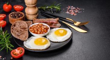 English breakfast with fried eggs, bacon, beans, tomatoes, spices and herbs photo
