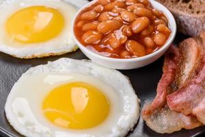 desayuno inglés con huevos fritos, tocino, frijoles, tomates, especias y hierbas foto