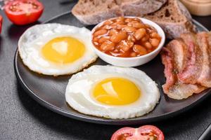 English breakfast with fried eggs, bacon, beans, tomatoes, spices and herbs photo