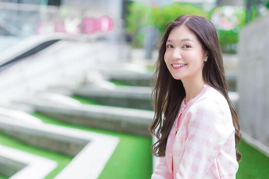 Asian beautiful woman in a pink and white striped coat is sitting at the green grass and stair as a background. photo