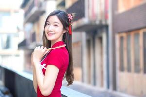 Beautiful Asian female in red dress stands holds a fan among old city center in Chinese new year theme. photo