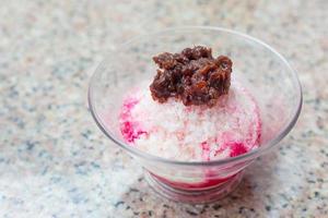 postre tradicional japonés, un tazón de frijol rojo dulce con hielo rojo estaba encima con leche condensada y puesto sobre una mesa de granito. foto