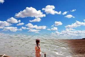 Portrait of a beautiful girl standing on a boat and looking distance over the beach and mountain with white clouds, a blue sky. Traveling concept. photo