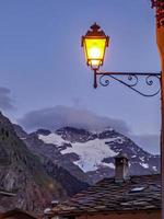 A vertical shot of an illuminated vintage lamp near snowy mountains