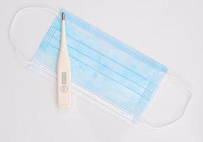 Close-up of surgical medical mask and thermometer on white background photo