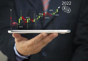 Businessman holding tablet 2022 stock market forecast outlook in his hand, charts and candlesticks, stock market movement trend, past to present.