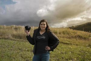 bella fotógrafa hispana con su cámara en la mano posando en medio del campo foto