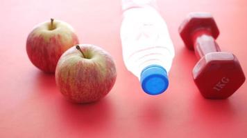 fresh drinking water, apple and a pink color dumbbell on red video