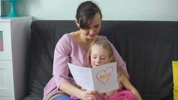 schattig klein meisje feliciteert haar moeder met moederdag. ze leest een tekst voor van haar zelfgemaakte wenskaart. gelukkig familieconcept video