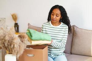 mujer afroamericana empacando ropa para donaciones benéficas en una caja de cartón en el salón
