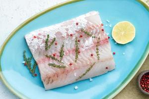 filete de pescado blanco crudo en un plato azul sobre un fondo blanco. pieza entera de pescado fresco foto