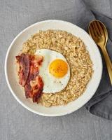 Oatmeal, fried egg and fried bacon. Hearty fat high-calorie breakfast, source of energy. Vertical photo