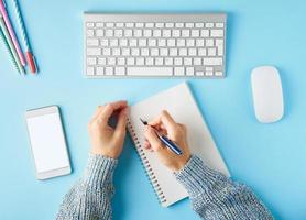 Faceless woman writing in notepad. Mobile phone with blank white screen display. photo