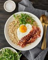 Oatmeal, fried egg, fried bacon. Balance of proteins, fats, carbohydrates. Balanced food. Vertical photo