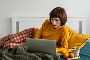 Mature woman laying on bed in bedroom and watching movie on laptop. photo