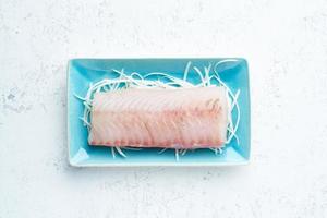 filete de pescado blanco crudo en un plato azul sobre un fondo blanco. foto