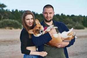 Young happy couple with dog standing on beach. Beautiful girl and guy and Corgi puppy having fun photo