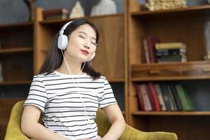 Young beautiful Asian girl listening to music with headphones sitting in chair photo