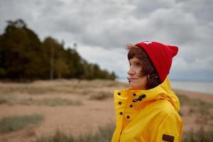 uno con la naturaleza. hermosa mujer madura mirando al bosque con chaqueta amarilla brillante y sombrero rojo foto