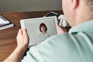 el hombre mira la tableta, la videollamada al médico, la comunicación con el médico en línea. telemedicina foto