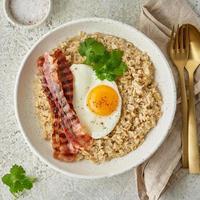 Oatmeal, fried egg, fried bacon. Hearty fat high-calorie breakfast, top view photo