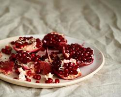 Still life with broken open pomegranate and seeds on plate on table covered with crumpled beige tablecloth