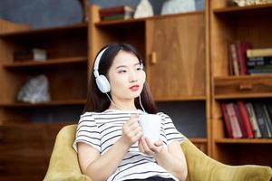 joven hermosa chica asiática escuchando música con auriculares sentados en una silla foto