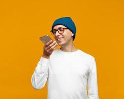 Portrait of positive young man recording audio message, speaking to microphone of mobile phone photo