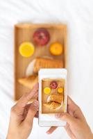 Blogger taking photos of food, shooting Breakfast in bed at hotel on mobile phone, tray with juice