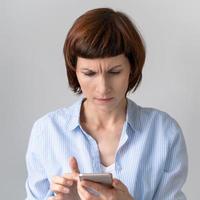 Middle-aged woman looking at phone and frowning. Wrinkle on forehead
