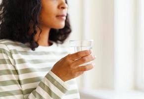 mujer afroamericana recortada bebiendo un vaso de agua. refrescante comienzo del día foto