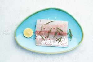 filete de pescado blanco crudo en un plato azul sobre un fondo blanco. pieza entera de pescado fresco foto
