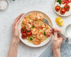 Pasta bavette with fried shrimps, bechamel sauce. Woman hands in frame, girl eats pasta, top view photo