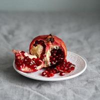 Still life with broken open pomegranate and seeds on plate on table covered with crumpled gray tablecloth photo