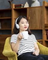Young beautiful Asian girl listening to music with headphones sitting in chair