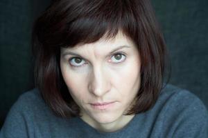 Woman looks from under her brows, frowning and stern. A serious face close up. Anger and wariness photo