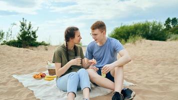 Young adult couple talking and having picnic on beach photo