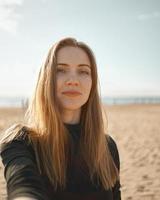 hermosa mujer con cabello largo, rubia tomando selfie en el teléfono móvil en la playa de arena en verano foto