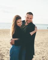 Young adult couple standing on coast and huging each other and looking away to someone. photo