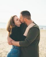 pareja de adultos jóvenes de pie en la costa y besándose. hombre sonriente guapo foto