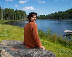 Back view of brunette lady in hat resting at lake in Karelia photo