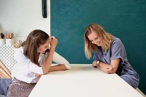 Two beautiful women laugh. Female businesswoman sit at table in workplace and talk, have fun photo