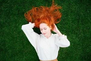 Beautiful girl with red hair lying on green grass with closed eyes photo