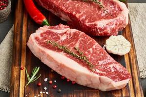 Seasoning raw steak with salt, thyme, garlic. Two big whole piece of raw beef meat photo