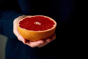Close-up of woman's hand holding fresh halved red bright citrus fruit grapefruit