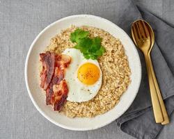 Oatmeal, fried egg and fried bacon. Hearty fat high-calorie breakfast, source of energy. photo